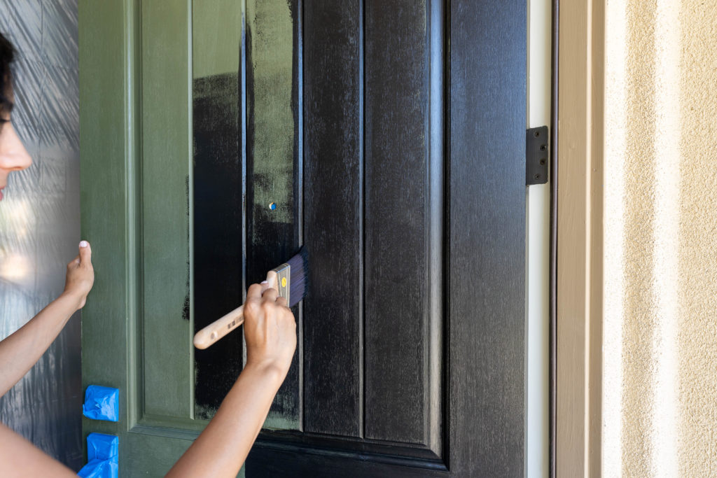Woman painting green front door black with Behr Ultra Exterior in Limousine Black