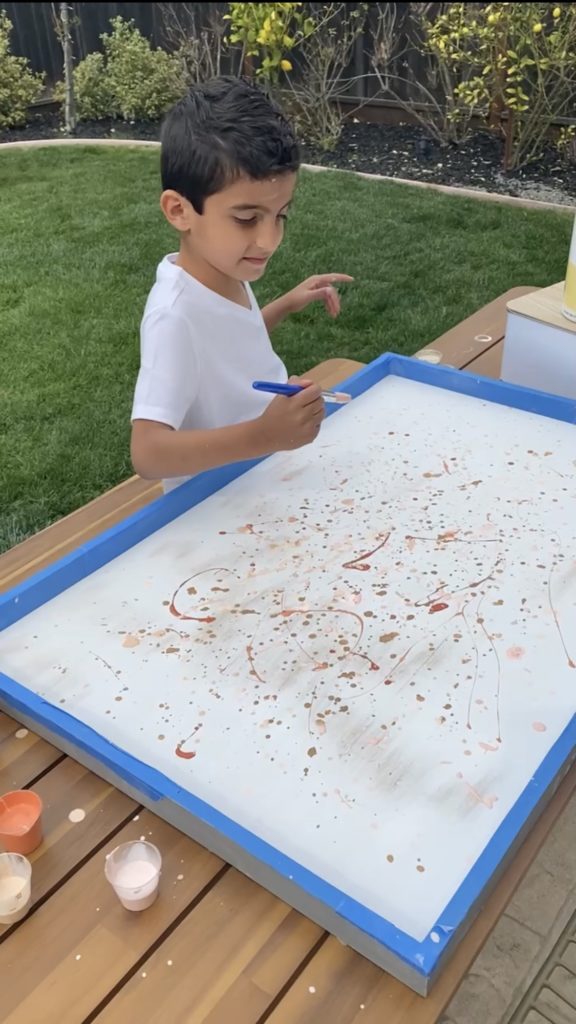 Young child creating a Jackson Pollock inspired art using drip painting method