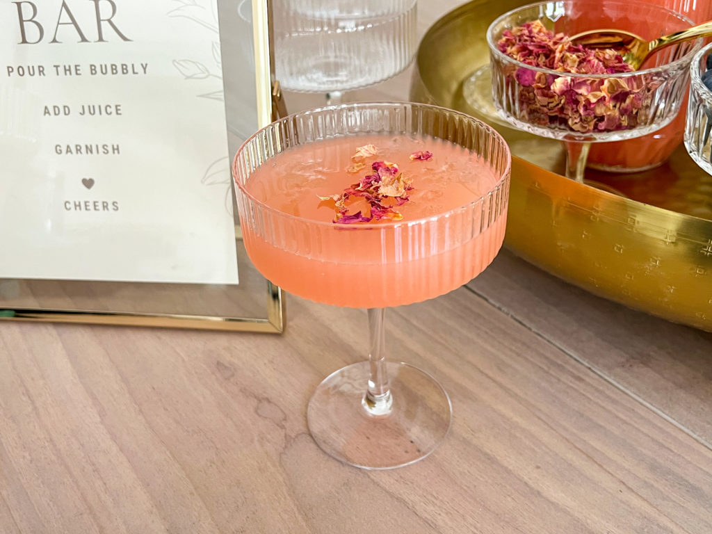 A fluted champagne coupe with a mimosa made from guava juice, champagne and rose petals