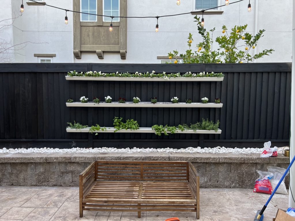 stained black fence with vertical garden made of gutters as planters