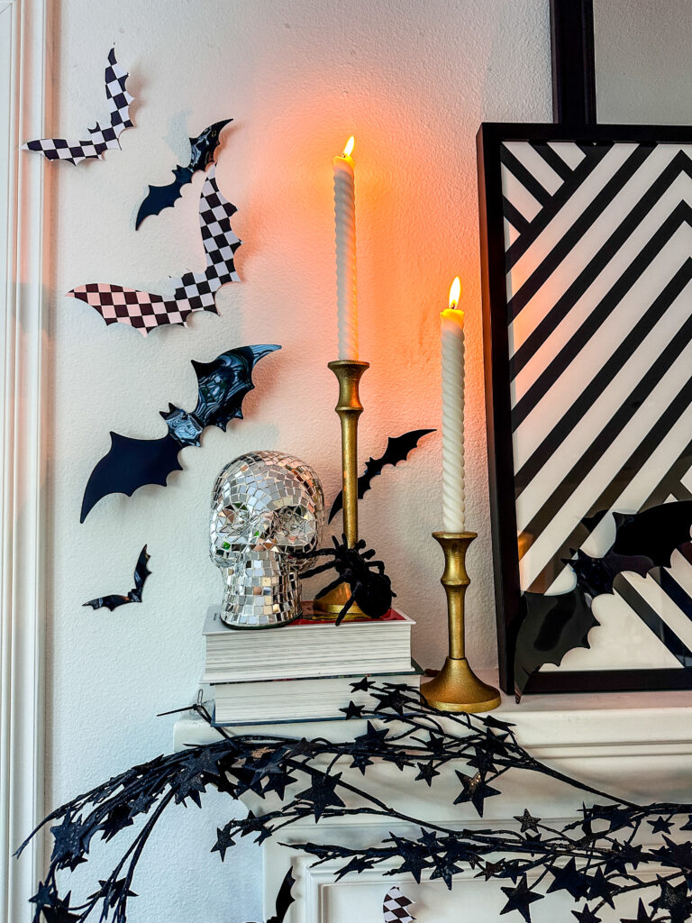 Black and white decorated Halloween mantle with checkered bats, black star garland, white ceramic ghosts, disco skull and lit taper candles