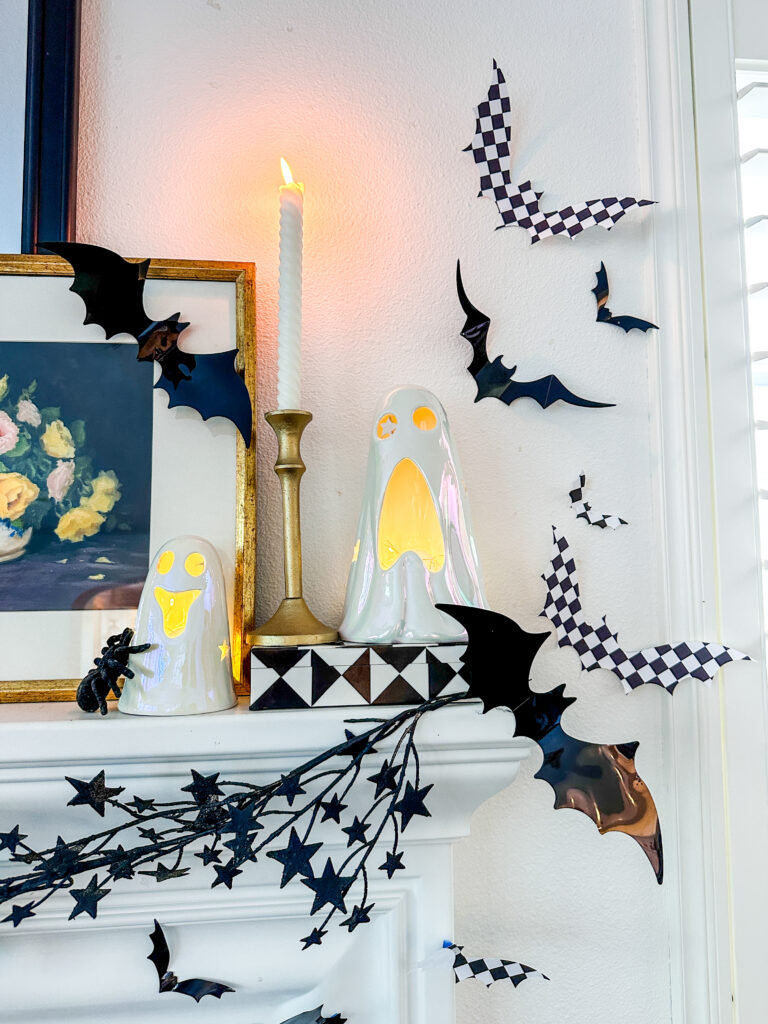 Black and white decorated Halloween mantle with checkered bats, black star garland, white ceramic ghosts and lit taper candle