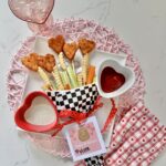 Plate with Valentine chicken nuggets that are heart shaped arranged as a bouquet with fries, celery and carrots/ There is a printable tag that saus " Nugs and Kisses "