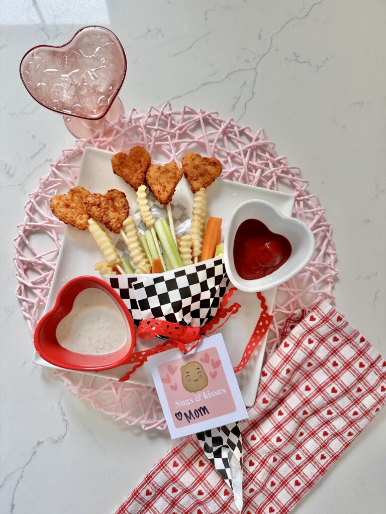 Plate with Valentine chicken nuggets that are heart shaped arranged as a bouquet with fries, celery and carrots/ There is a printable tag that saus " Nugs and Kisses "