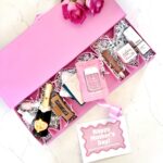 Mother's Day gift box that is pink and spells out Mom filled with mom's favorite things like cosmetics, mini bottle of champagne.