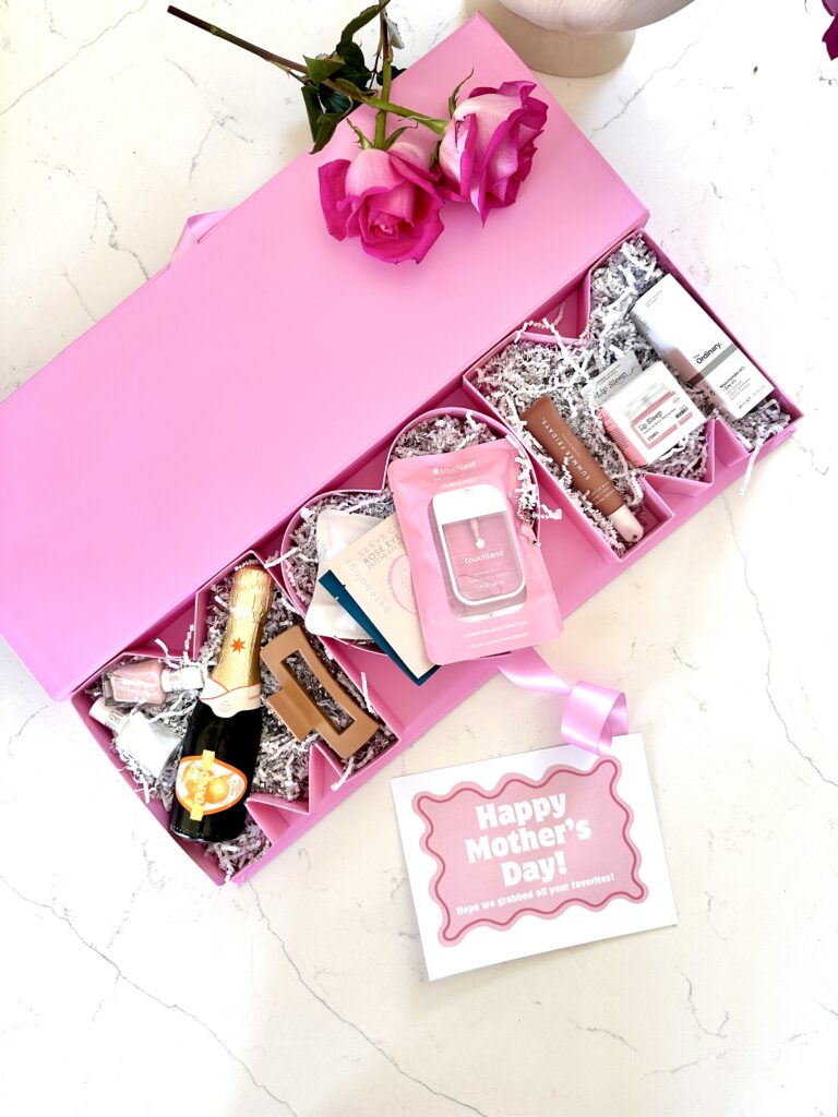 Mother's Day gift box that is pink and spells out Mom filled with mom's favorite things like cosmetics, mini bottle of champagne. 