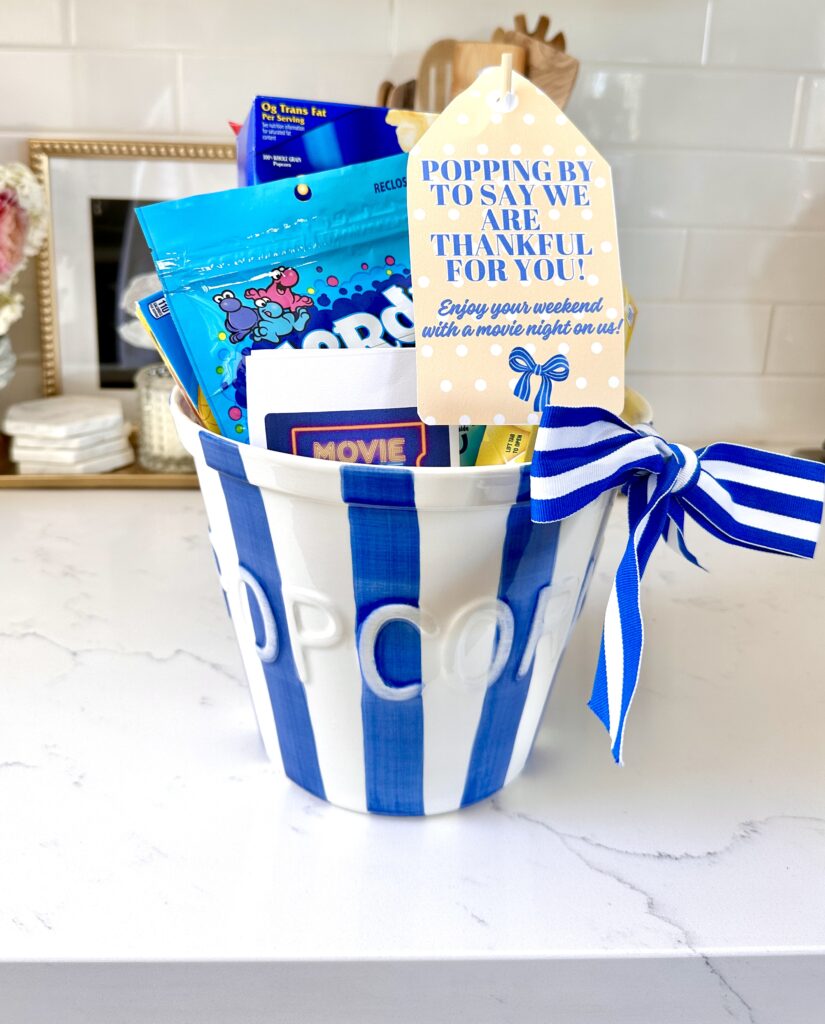 Teacher basket made for teacher appreciation back to school. It is a blue and white striped popcorn bucket filled with movie night essentials and a tag that says popping by to say "We are thankful for you! Enjoy your weekend with a movie night on us!"