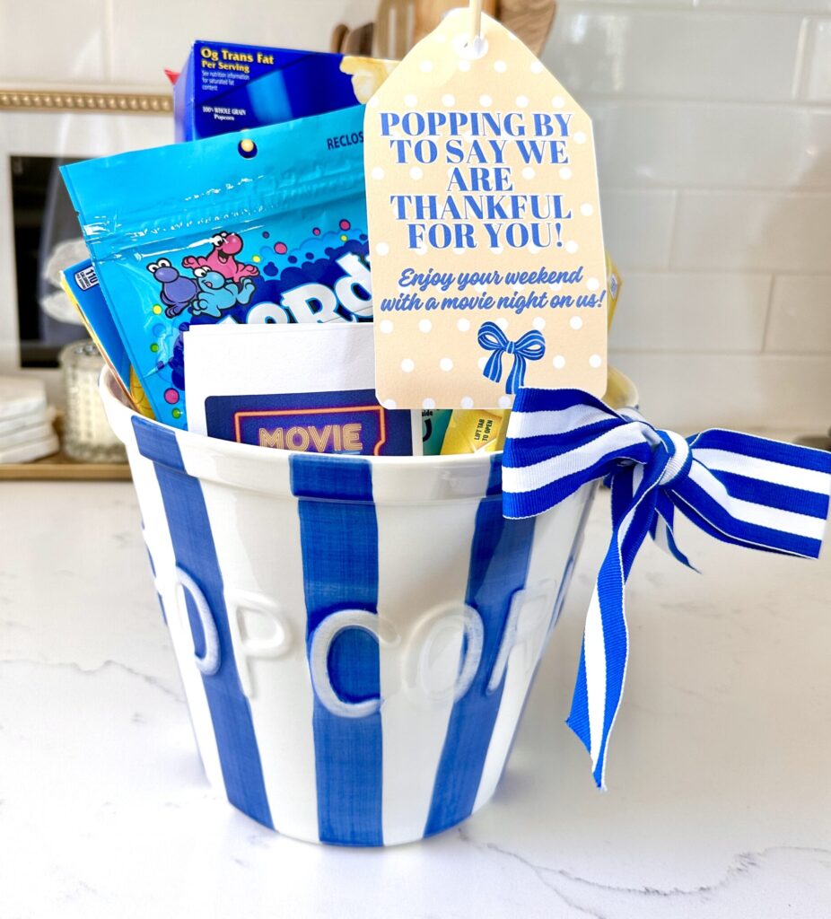 Teacher basket made for teacher appreciation back to school. It is a blue and white striped popcorn bucket filled with movie night essentials and a tag that says popping by to say "We are thankful for you! Enjoy your weekend with a movie night on us!"